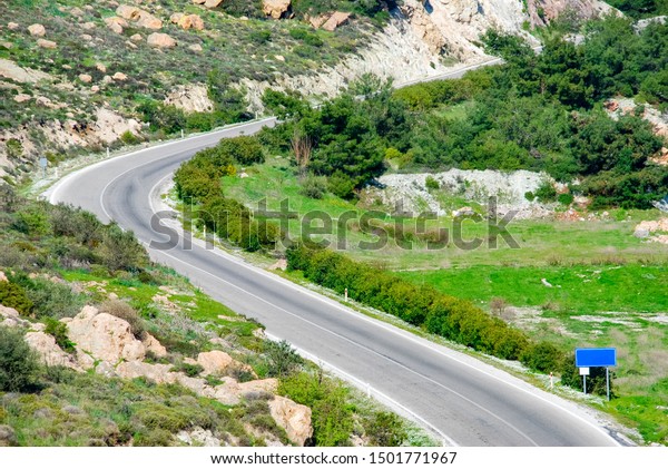 S curved road with road sign, through the\
mountain landscape.