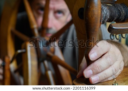 S3niorLife. Skilled tradesman looks to repair and to intricately fettle the mechanism of an old wooden spinning wheel. Selective focus to accentuate the task of repair. 