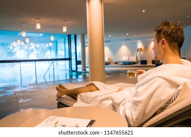 Saalbach hotel. Austria. March 20, 2018. Young man having a rest in the SPA by the open pool in a robe. Reading magazine.