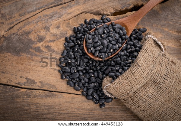 Sack of black beans spill beans with black\
beans in a wooden spoon on wooden\
table.