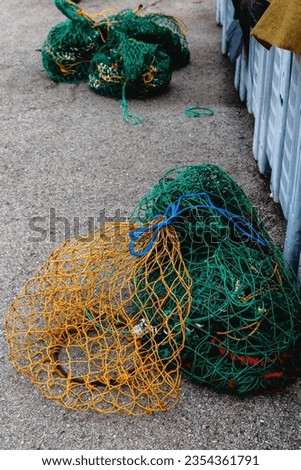 Sacks of fishing nets and green and yellow ropes piled on the floor of a harbor. Close up vertical image