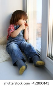 Sad 2 years boy sits on sill and looks out of window in wintertime