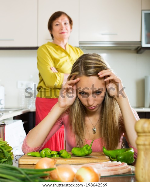 Sad adult daughter and mature mother after\
conflict  in home kitchen