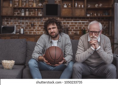 Sad Adult Son And Senior Father Watching Basketball Game At Home