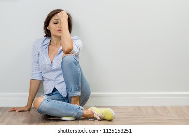 Sad adult woman in depression sits on the floor of the house, closed her eyes, holds her head in her hand. - Powered by Shutterstock