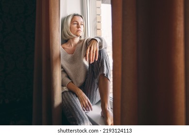 Sad adult woman look in window distance thinking or pondering alone at home, thoughtful upset unhappy middle aged female lost in thoughts dreaming, feel lonely distressed, loneliness concept