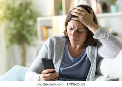 Sad Adult Woman Reading Bad News On Smart Phone Sitting On A Couch At Home