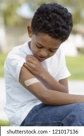 Sad African American Boy Looking At Band Aid On His Arm