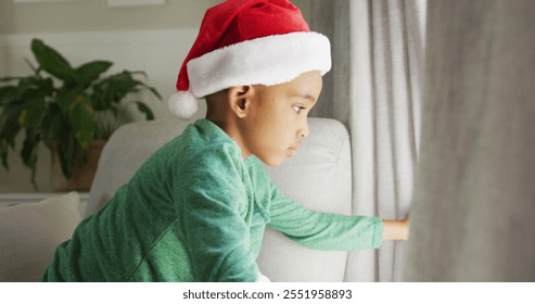 Sad african american boy wearing santa hat looking outside window at christmas time. christmas, festivity and tradition at home. - Powered by Shutterstock