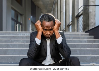 Sad african american businessman sitting on stairs outside office building, man in business suit bankrupt fired from job, boss lost money. - Powered by Shutterstock