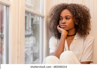 Sad African American Girl Sitting On The Windowsill And Looking Out Of The Window.