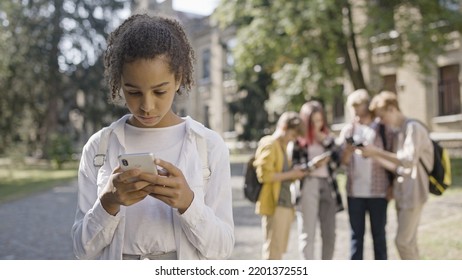 Sad African American Girl Suffering From Social Media Bullying From Group Of School Children