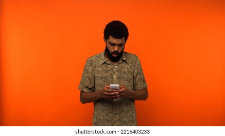 Sad African American Man Using Smartphone On Orange Background