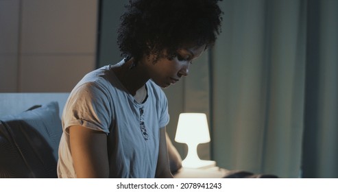 Sad African American Woman Sitting On Bed At Night, She Can't Sleep