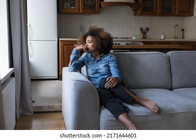 Sad African teen girl sit on sofa lost in thoughts, thinks staring into distance, looks upset experiences first unrequited love, having low self-esteem, problems, feels insecure. Teen problem concept