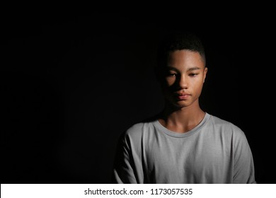 Sad African-American teenage boy on dark background
