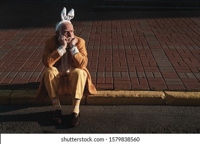 Sad aged male sitting on road in coloured suit and bunny hairband. Website banner