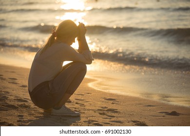 Sad And Alone Young Woman Sitting On The Beach At Sunset.