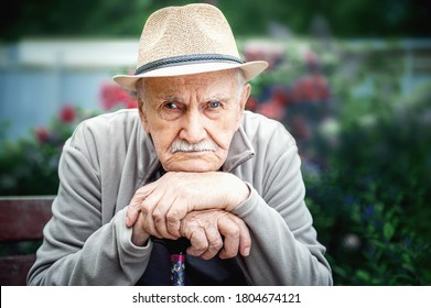sad, angry old man with a hat is sitting in an open-air garden. concept of loneliness and lonely old age