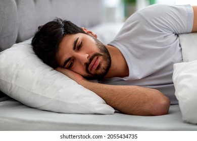 Sad arab guy lying alone in bed, suffering from loneliness and thinking of problems. Male stress and depression, sleeplessness and apathy concept.