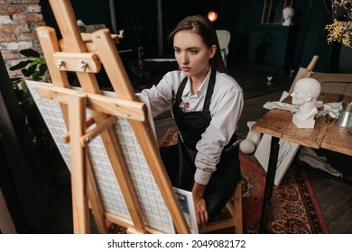 A sad artist paints on canvas at an art school. Portrait of the artist in the studio.