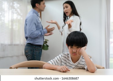 Sad Asian Boy Sitting Alone In Dining Table While Parents Quarreling Behind His Back At Home.problem In Family And Bad Relations