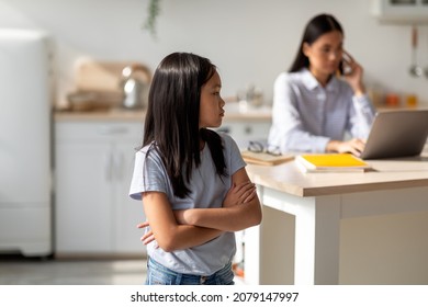 Sad Asian Girl Taking Offence At Her Busy Mother Working Online On Laptop Computer From Home, Free Space. Child Feeling Neglected And Lonely With Her Mom Having Remote Job