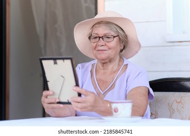 Sad Asian Grandma Looks At Framed Photo. Nice Memories. An Elderly Woman Lovingly Looks At The Photo.