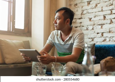 Sad Asian Man Using Tablet Computer Sitting at Cafe Depressed Looking to Window - Powered by Shutterstock