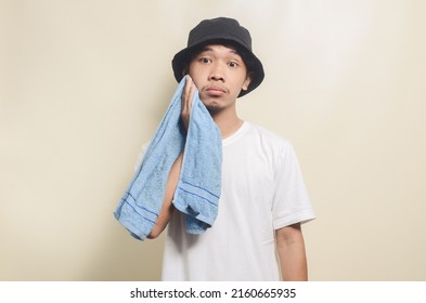 Sad Asian Man Wearing Bright White T-shirt With Black Hat And Carrying Towel On Isolated Background