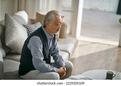 sad asian senior man sitting on couch in living room at home