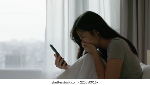 sad asian woman look smart phone feeling depressed of receiving internet bullying message or email with bad news sit on bed in bedroom at home