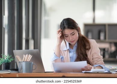 Sad Asian woman looking annoyed and stressed, sitting at the desk, using a laptop, thinking, feeling tired and bored with depression problems - Shutterstock ID 2254525369