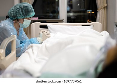 Sad asian woman or nurse in face mask and medical uniform,pray with closed eyes,hands clasped together,say a prayer for senior patient lying in the hospital bed,take care,look after of the old elderly