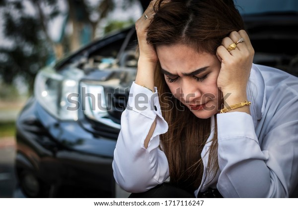 Sad Asian woman sitting on the\
road near her accident broken car black talking on the\
phone.\
