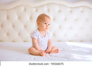 Sad Baby In White Sunny Bedroom.