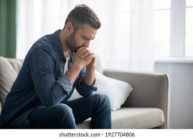 Sad bearded middle-aged man in casual sitting on couch at home, leaning on hands and looking down, upset man having problems, side view, copy space. Loneliness, depression, financial hangover concept