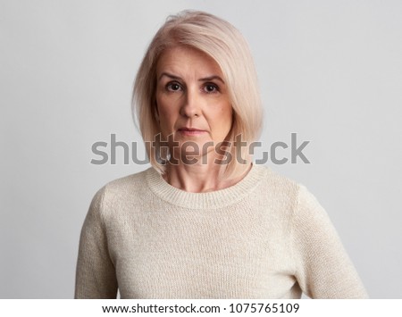 sad beautiful aged woman wearing sweater over grey studio wall. Old granny