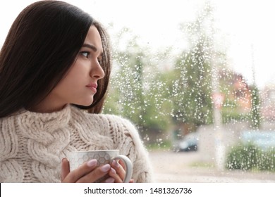 Sad Beautiful Woman With Cup Near Window Indoors On Rainy Day