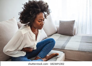 Sad beautiful woman sitting on the couch and feeling spasm and symptoms of pms. Shot of a young woman experiencing stomach pain on the sofa at home