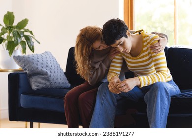 Sad biracial lesbian couple embracing and comforting sitting on couch at home, copy space. Depression, mental health, support, care, gay, relationship, togetherness and domestic life, unaltered. - Powered by Shutterstock