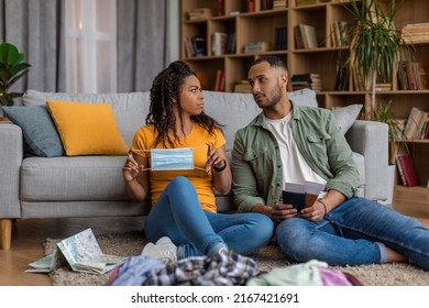 Sad Black Couple Preparing For Vacation, Man Holding Passport With Flight Tickets, Woman Showing Face Mask, Packing Suitcases For Trip. Vacation Travel And Tourism During Pandemic