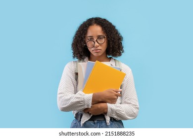 Sad Black Female Student Feeling Tired, Holding Notebooks On Blue Studio Background. Exhausted Young African American Woman Getting Ready For College Or University Exam, Overworking During Classes