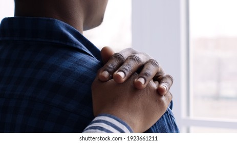 Sad black man looking at window at home during pandemic outbreak, his wife touching his shoulder, comforting him, back view, slow motion - Shutterstock ID 1923661211