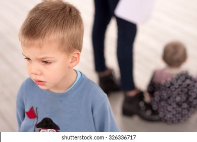 Sad Blond Boy Jealous About Being Neglected By His Mother Or Caregiver Who Is Giving Attention To Another Child