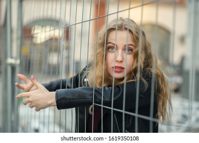 Sad Blond Girl Prisoner Behind Bars Looking At Camera