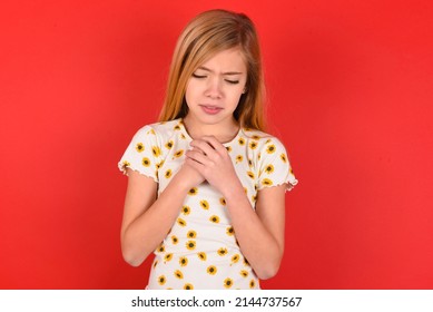 Sad blonde little kid girl wearing daisy t-shirt over red background desperate and depressed with tears on her eyes suffering pain and depression  in sadness facial expression and emotion concept
