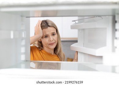 Sad Blonde Woman In Casual Looking Inside Open Empty Fridge And Touching Her Head, Lack Of Food, Need For Shopping, Suffering From Financial Hangover While Pandemic, Copy Space