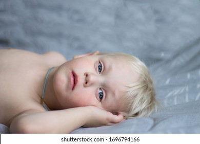 Sad  Blue-eyed Blonde Child Looking At The Camera Lying On The Sofa