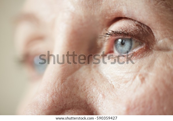 Sad blue-grey eyes of elderly woman looking\
to the side, extreme close-up\
shot